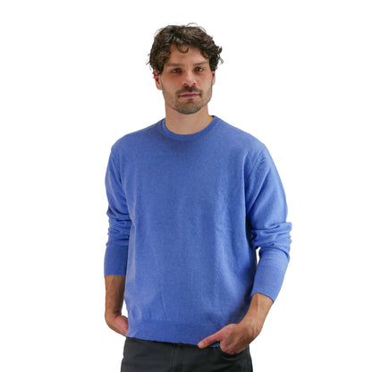 Das Model trägt einen Pullover mit Rundhalsausschnitt die Farbe ist denim. Frontansischt, hat die Hände in der Hose. 